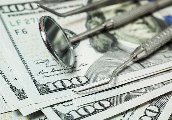 A set of dental tools laying on a pile of hundred-dollar bills