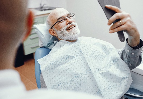 Man smiling at reflection in handheld mirror in treatment room