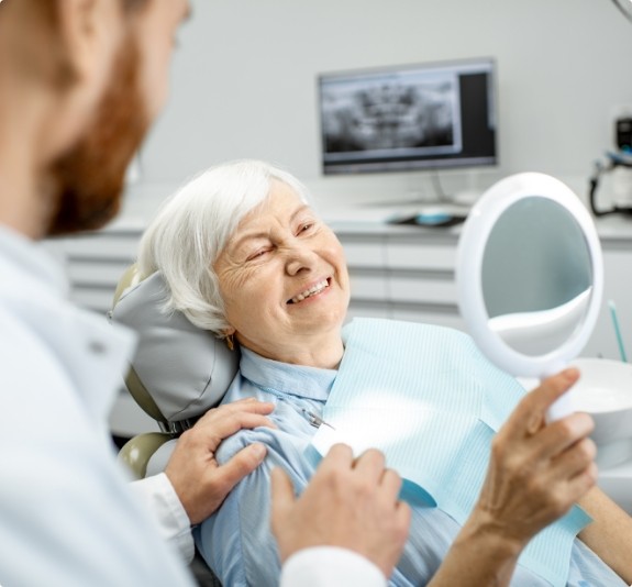 Senior woman in dental chair admiring her smile in mirror