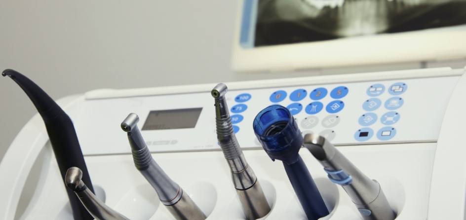 Row of dental instruments with x ray of teeth on screen in background