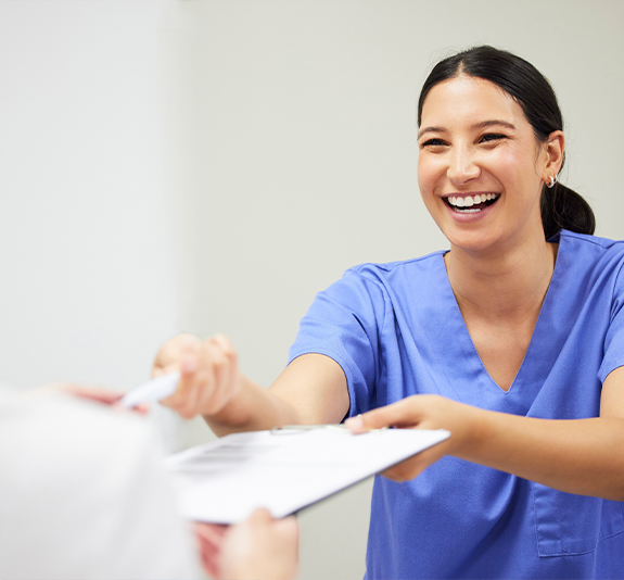 Smiling dental team member handing a clipboard to a patient
