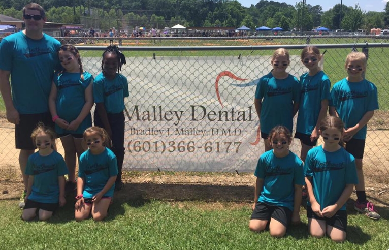 Doctor Malley with girls sports team in front of fence with Malley Dental sign