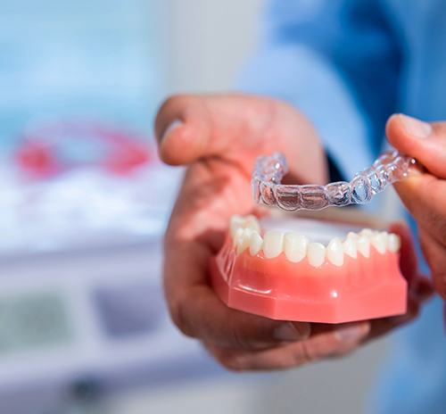 Dentist placing a clear aligner on a model of teeth
