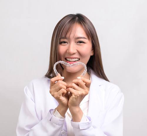 Woman smiling while creating a heart shape with two clear aligners