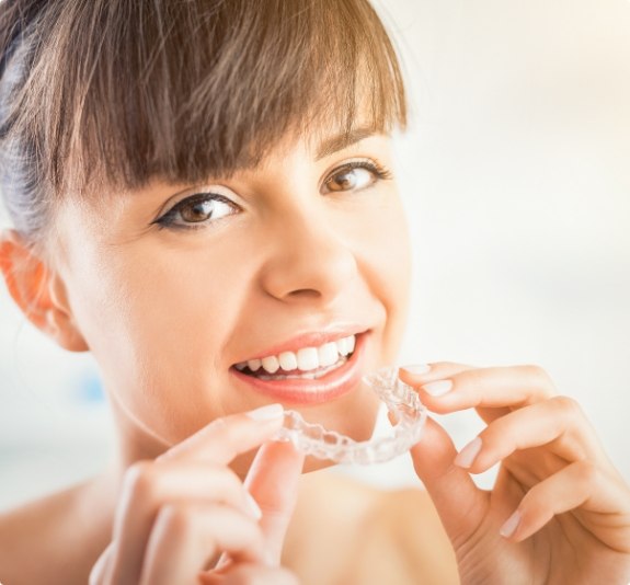 Smiling woman holding Invisalign clear aligner