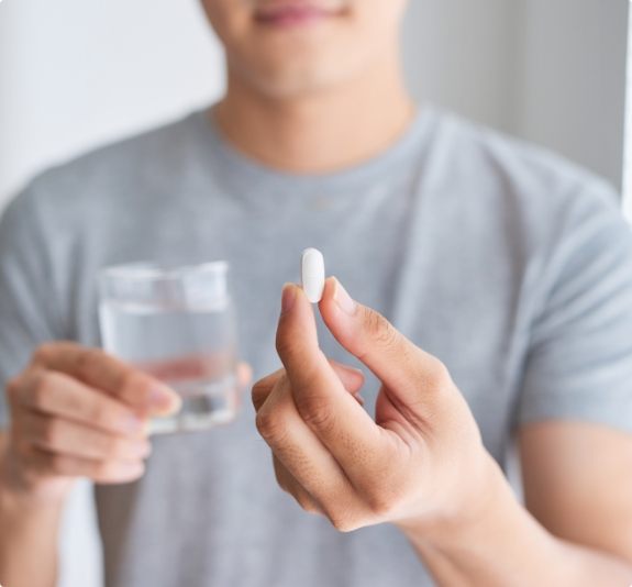 Man holding a pill and a glass of water